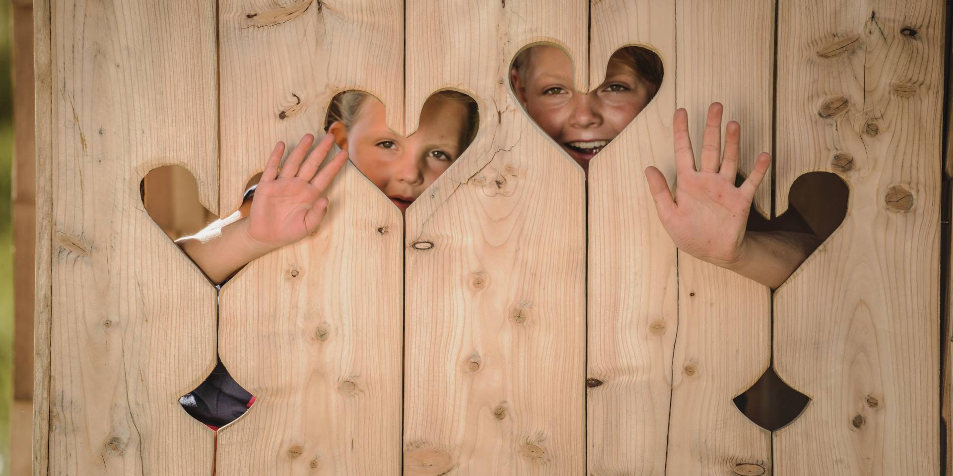 Children behind wooden wall with hearts waving out