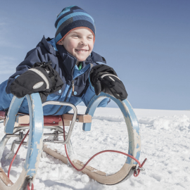 Boy laughing while sledding during a winter holiday in Maria Alm, Hochkönig region.