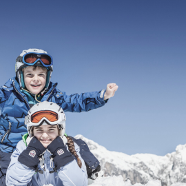 Two kids having fun in the snow under a bright blue sky during a family winter holiday in Maria Alm.