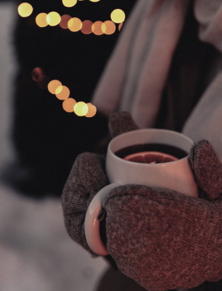 Glühwein in der Hand mit warmen Handschuhen, stimmungsvolle Winterlichter im Hintergrund im Hotel die HOCHKÖNIGIN in Maria Alm