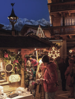 Ein Pärchen schlendert über den stimmungsvollen Weihnachtsmarkt in Maria Alm mit festlich geschmückten Holzhütten, leuchtenden Lichtern und winterlicher Bergkulisse nahe dem Hotel die HOCHKÖNIGIN