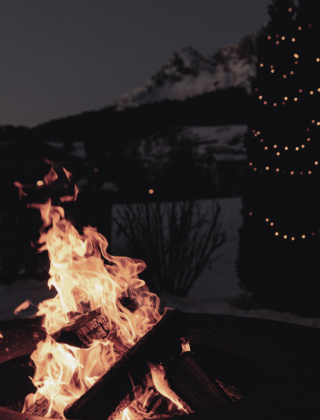 Am Abend lodert ein offenes Feuer auf der Terrasse des Hotels die HOCHKÖNIGIN im Salzburger Land, daneben steht ein geschmückter Tannenbaum mit Lichtern und im Hintergrund erheben sich die Berge mit Blick bis zum Steinernen Meer