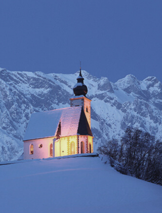 Kirche in Dienten während der Adventszeit in der Abenddämmerung, umgeben von Schnee und mit den Bergen im Hintergrund, stimmungsvolle Winteratmosphäre nahe dem Hotel die HOCHKÖNIGIN