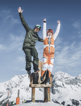Two winter holiday guests enjoying a sunny summit experience with panoramic views over the Hochkönig.