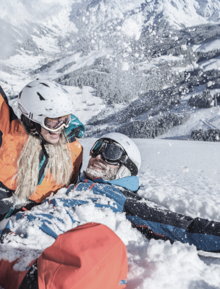 Couple laughing in the snow with the snowy Hochkönig mountains in the background – pure winter joy in Maria Alm.