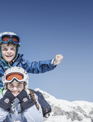 Zwei Kinder haben Spaß im Schnee bei strahlend blauem Himmel im Familienurlaub in Maria Alm.