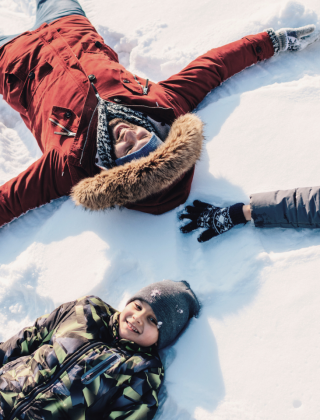 Familie liegt lachend im Schnee und formt Schneeengel beim Winterurlaub im Salzburger Land.