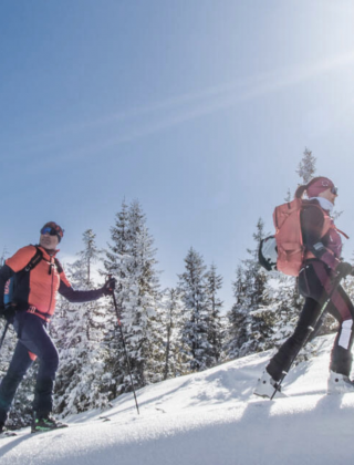 Two ski tourers enjoy the snow-covered mountain landscape of the Hochkönig under bright sunshine – active winter holiday in Maria Alm.