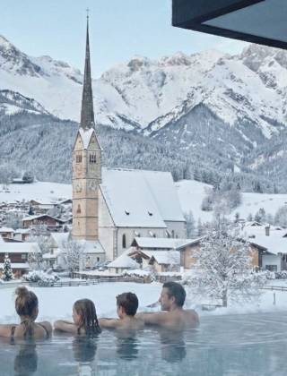 Winter view from the infinity pool of Hotel Die Hochkönigin overlooking Maria Alm and the Hochkönig mountains – luxury wellness hotel in the Austrian Alps with pool and panoramic views.