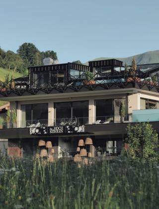 Hotel die HOCHKÖNIGIN in Maria Alm mit TIARA SPA und Infinitypool vor der Berglandschaft der Hochkönig-Region im Salzburger Land.