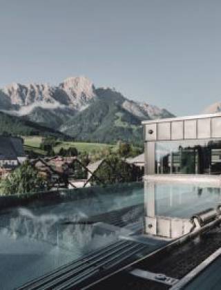 Infinity pool at the TIARA SPA at Hotel die HOCHKÖNIGIN in Maria Alm at Hochkönig overlooking the village church and surrounding mountain landscape.