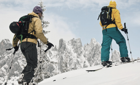 Two ski tourers ascend through fresh powder snow with a view of the rugged Hochkönig peaks.