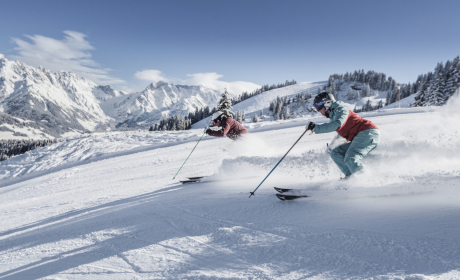 Zwei Skifahrer gleiten mit voller Geschwindigkeit durch den Pulverschnee am Hochkönig – Sonnenschein, Panorama und pures Skivergnügen in Maria Alm.