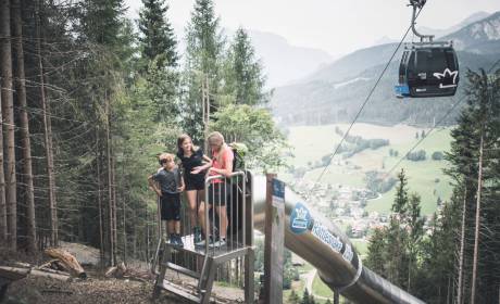 Familie am Waldrutschenpark am Hochkönig bei Maria Alm mit Blick ins Tal und Gondelbahn – Erlebnis für Kinder und Familien in den Bergen.