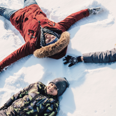 Family laughing in the snow making snow angels during a winter holiday in Salzburg, Austria.