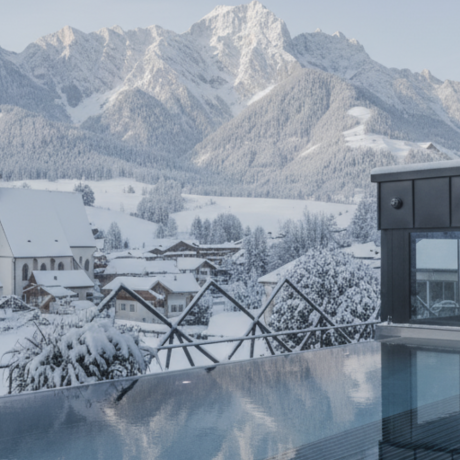 Rooftop spa with infinity pool at Hotel die HOCHKÖNIGIN offering a stunning winter view of Maria Alm and the Hochkönig mountains in Salzburg.