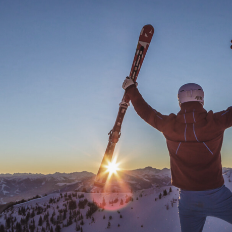 A skier raises their arms in joy at sunrise over the snowy mountains of the Hochkönig.