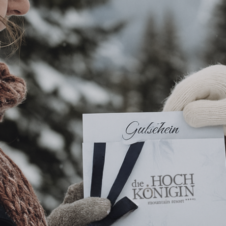 Two people exchange a HOCHKÖNIGIN gift voucher in snowy alpine scenery – a warm and heartfelt winter gift idea from Maria Alm, Austria.
