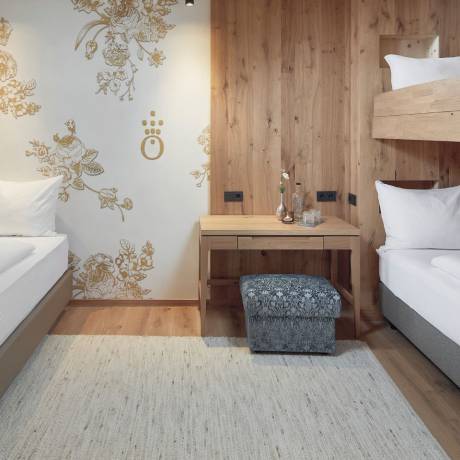 Modernes Familienzimmer im Hotel die HOCHKÖNIGIN in Maria Alm mit hellem Holz, Etagenbett, Einzelbett und stilvollen Details – gemütlicher Rückzugsort für Familienurlaub am Hochkönig.