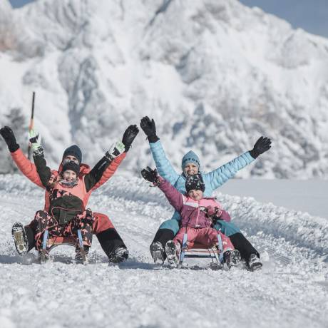 A family enjoying a fun sledding adventure in the snowy mountains of Maria Alm. Bright sunshine, fresh powder and joyful moments create the perfect winter experience for guests of the HOCHKÖNIGIN.