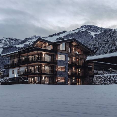 Winter exterior shot of the HOCHKÖNIGIN in Maria Alm, surrounded by snow-covered peaks and warm glowing lights. The perfect setting for a relaxing winter escape in the Austrian Alps.