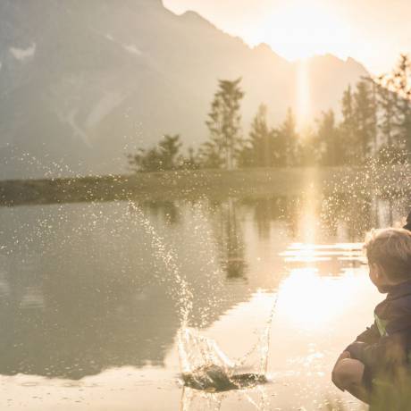 Familie am Bergsee bei Sonnenuntergang am Hochkönig in Maria Alm, Kinder spielen am Wasser und genießen die Natur.
