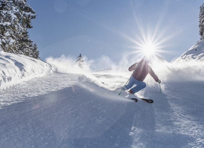 Skier carving smoothly through fresh powder under the bright winter sun at Hochkönig ski area in Salzburg.