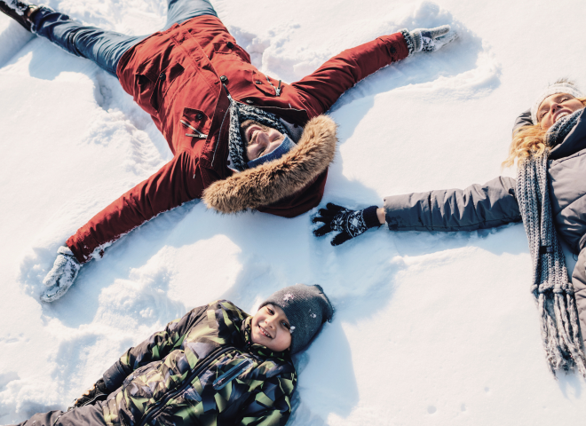Family laughing in the snow making snow angels during a winter holiday in Salzburg, Austria.