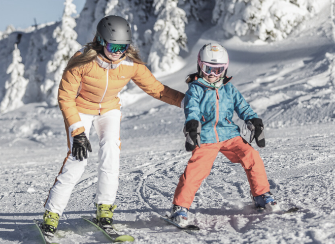 Mother helping her child learn to ski on the snowy slopes at Hochkönig.