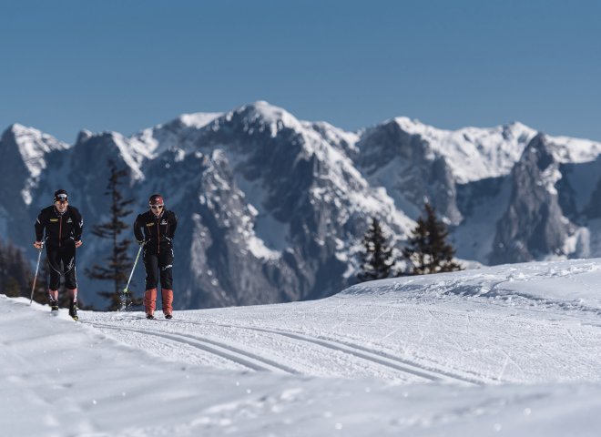 Two cross-country skiers gliding through the snowy winter landscape with a view of the Hochkönig mountains.