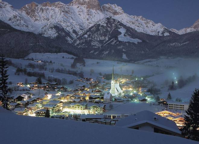 Winter evening in Maria Alm with snow-covered houses, church and the Hochkönig mountain range – magical alpine scene near the HOCHKÖNIGIN Hotel.