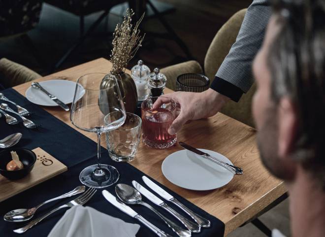 Stilvoll gedeckter Tisch mit Getränkeservice im Gourmetrestaurant des Hotels die HOCHKÖNIGIN in Maria Alm – exklusive Kulinarik in eleganter Atmosphäre.