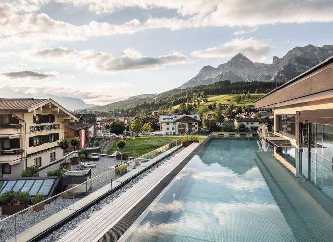 Infinitypool im QUEEN SPA des Hotels die HOCHKÖNIGIN in Maria Alm am Hochkönig mit Blick auf die Dorfkirche und die umliegende Berglandschaft.
