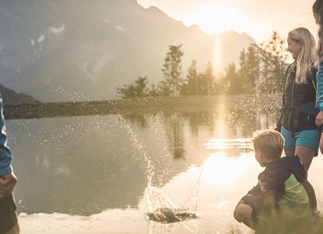 Familie am Bergsee bei Sonnenuntergang am Hochkönig in Maria Alm, Kinder spielen am Wasser und genießen die Natur.