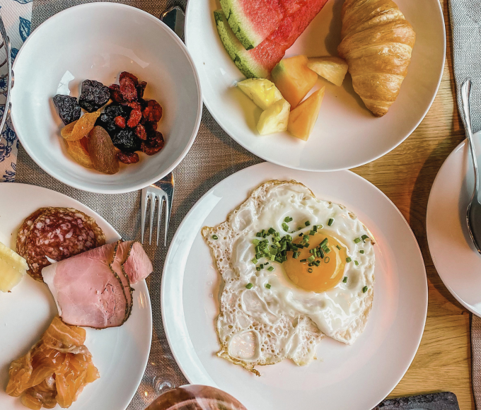 Gedeckter Frühstückstisch mit Kaffee, Spiegelei, Obst, Nüssen und vielem mehr