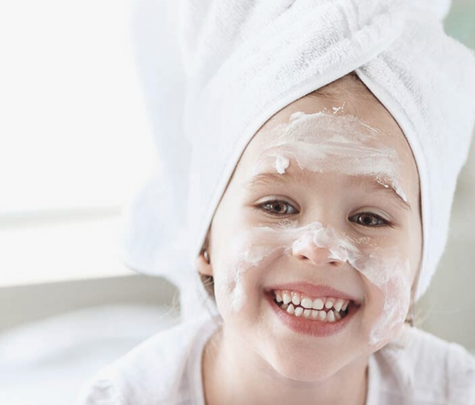 Little girl doing cosmetics with turban towel, mask on her face 