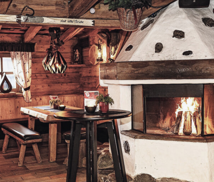Dengl Alm in Maria Alm mit offenem Holzofenfeuer, rustikalen Holzbänken und Tischen im alpinen Flair des Salzburger Landes