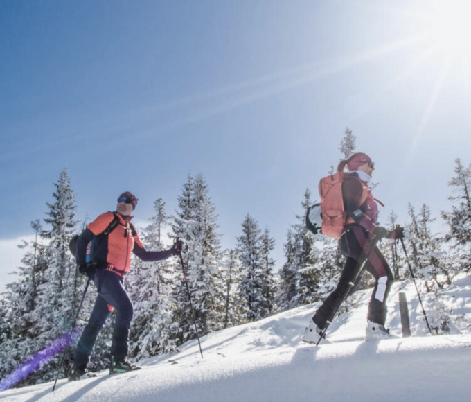 Two ski tourers enjoy the snow-covered mountain landscape of the Hochkönig under bright sunshine – active winter holiday in Maria Alm.