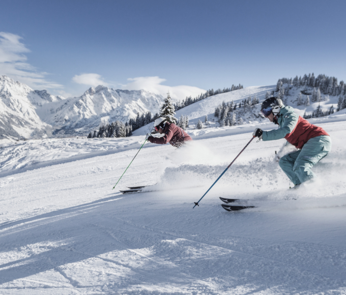 Zwei Skifahrer gleiten mit voller Geschwindigkeit durch den Pulverschnee am Hochkönig – Sonnenschein, Panorama und pures Skivergnügen in Maria Alm.