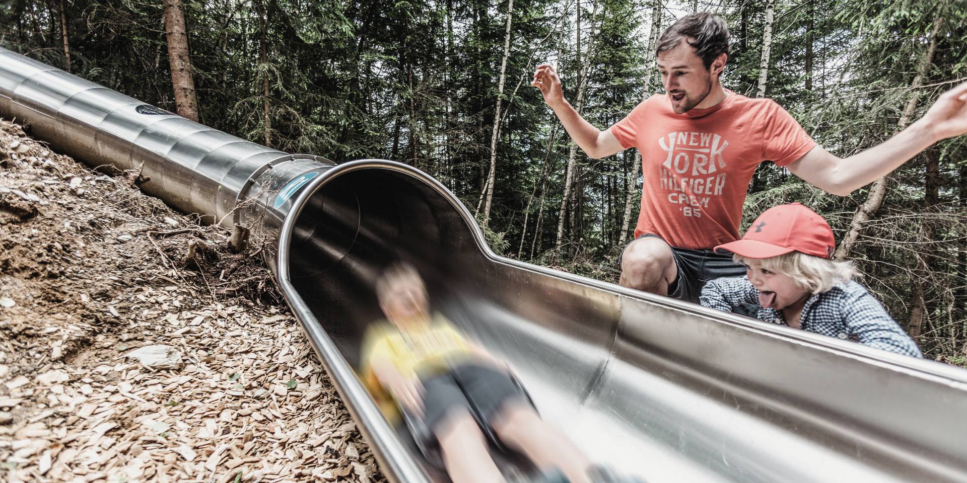 Kind beim Rutschen durch den Wald mit Vater und Bruder