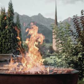 Fire bowl with a view from the terrace of the HOCHKÖNIGIN of the church of Maria Alm and the surrounding mountain world