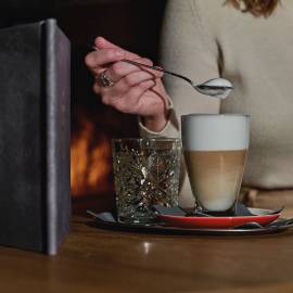 Woman in the lounge by the fireplace of the HOCHKÖNIGIN with a cafe latte