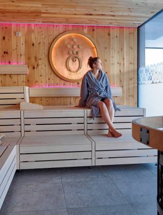  Frau mit Bademantel sitzt in Panorama Sauna
