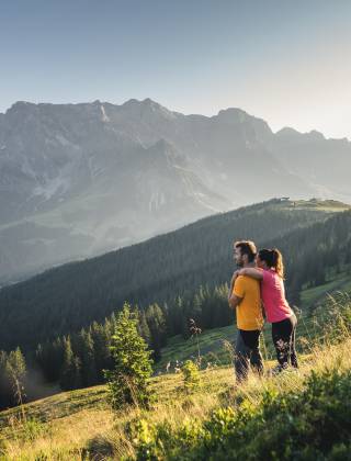 Frau umarmt Mann von hinten auf Bergwiese