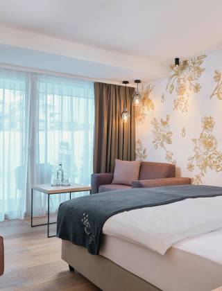 Bett im Hotelzimmer der HOCHKÖNIGIN mit stylischen Lampen und edler Tapete mit goldenen Blumen