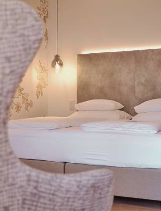 Bed in the hotel room of the HOCHKÖNIGIN with stylish lamps and noble wallpaper with golden flowers