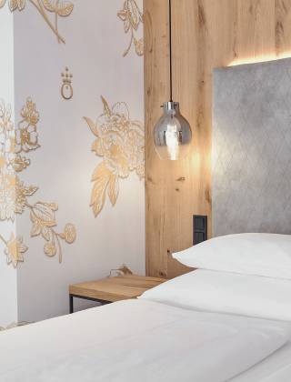 Bed in the hotel room of the HOCHKÖNIGIN with stylish lamps and noble wallpaper with golden flowers