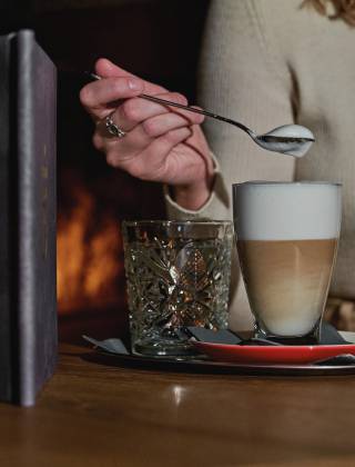 Woman in the lounge by the fireplace of the HOCHKÖNIGIN with a cafe latte