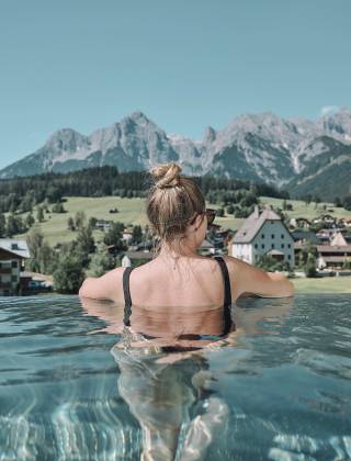 Frau im Infinity Pool mit fantstischer Aussicht auf die umligende Bergwelt