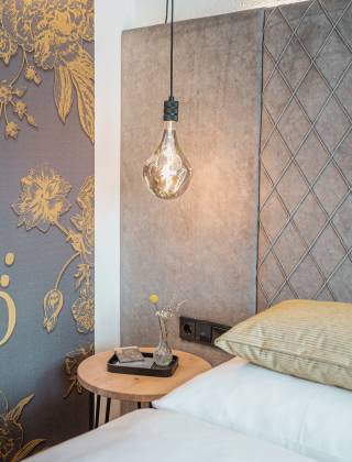 Partial view of the room in the HOCHKÖNIGIN with stylish wallpaper, lamp and bed